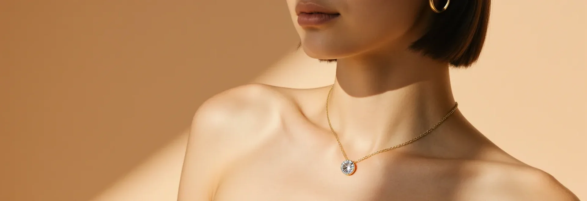 A model wearing a fine gold chain necklace with a crystal-pendant and a gold hoop earring, warm editorial light.