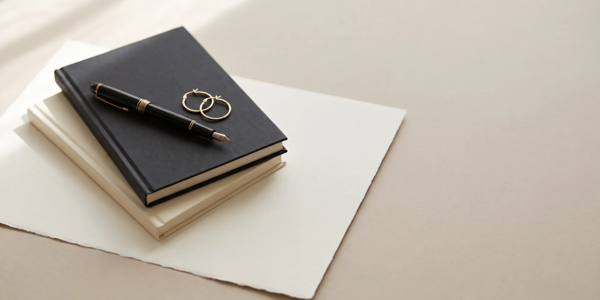 ALVANY press: gold hoop earrings and a fountain pen on two closed journals