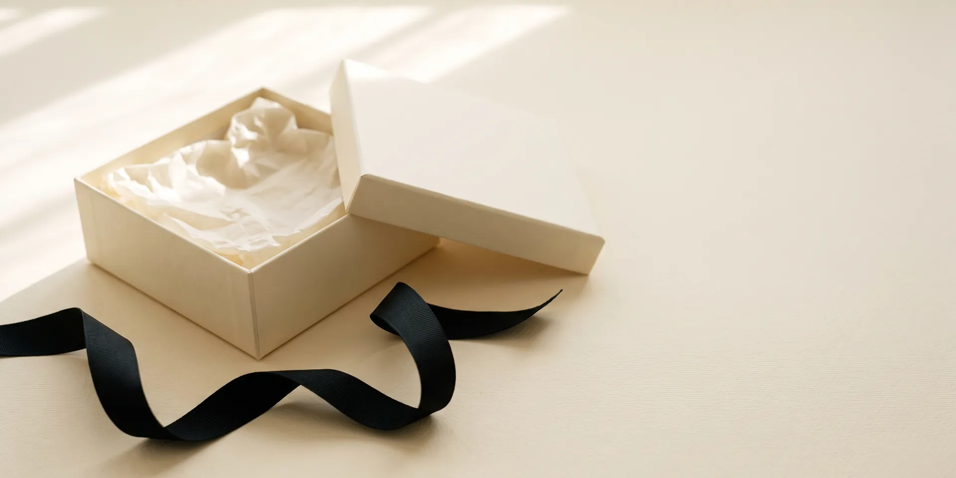 ALVANY returns — an open ivory box with tissue paper and a loose black ribbon